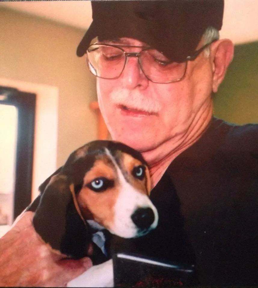 Older man in a baseball cap smiling and holding a beagle puppy
